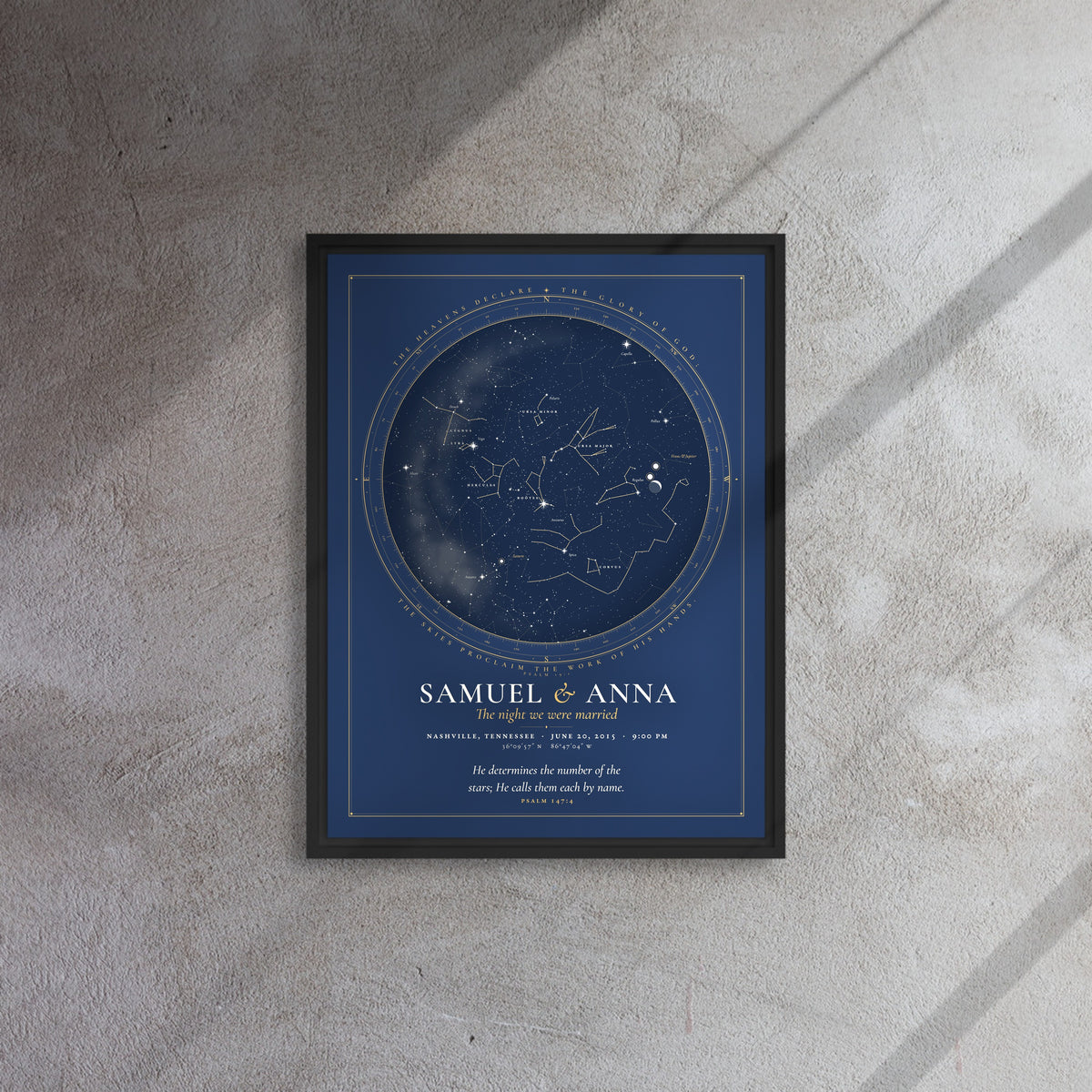 Framed canvas print of a night sky chart in a black floating frame, names Samuel and Anna, hung on a concrete wall