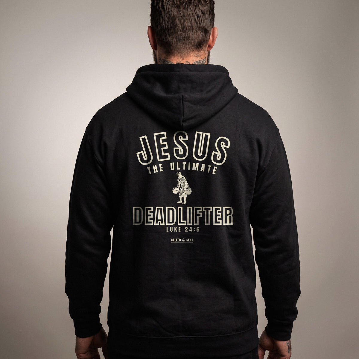Jesus the Ultimate Deadlifter Christian hoodie, Black, worn by a man, back view, Luke 24:6 varsity print with Called and Sent sign-off
