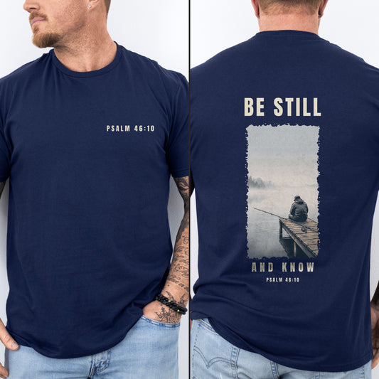 Be Still And Know Christian fishing shirt, Navy, worn by a man, front chest verse badge with misty pier poster back print, Psalm 46:10